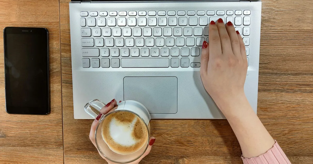 Dłonie piszące na laptopie obok filiżanki cappuccino, widok z góry