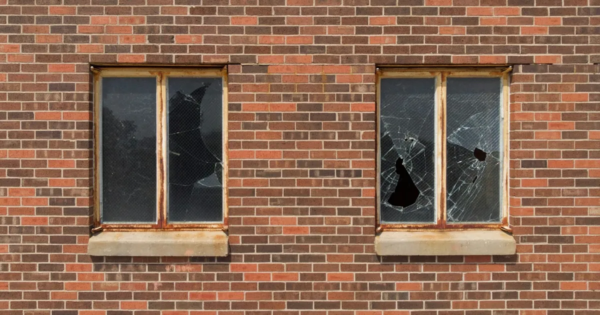 Two windows with broken glass in a brick wall