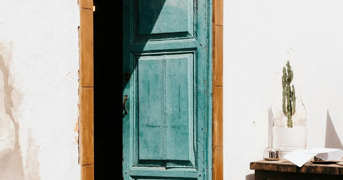 Open turquoise door in a white building wall